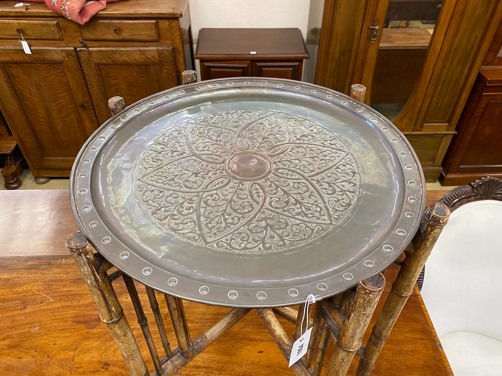 An early 20th century circular embossed copper tray on bamboo folding frame, diameter 58cm, height 67cm.